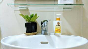 A bathroom sink with a glass shelf above it, a potted plant, a soap dispenser, and a mirror.