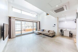 Amplia sala de estar con un gran ventanal corredero que da a un balcón, un sofá, una mesa de centro y una kitchenette.