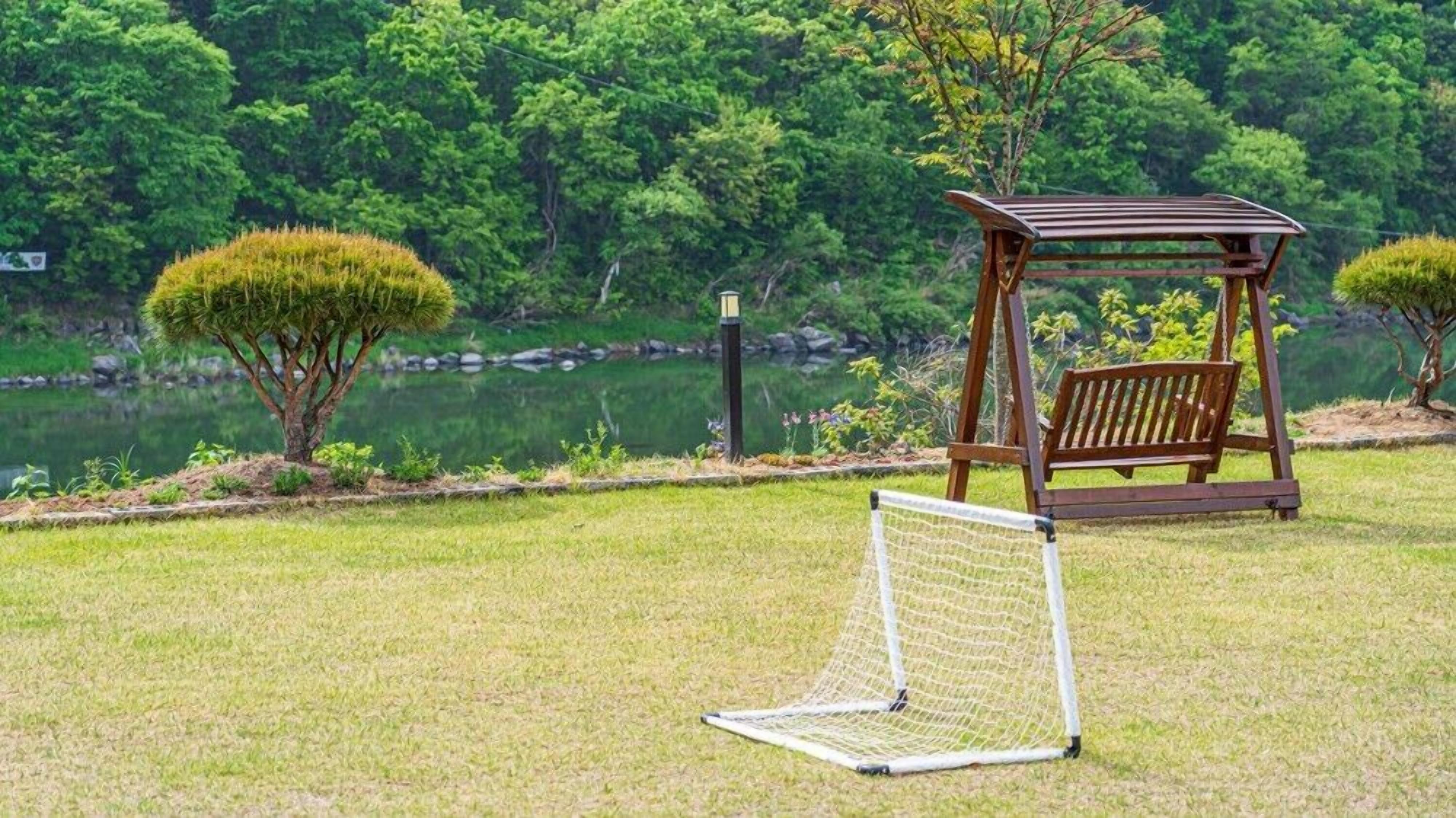 A gazebo with a bench, a goalpost, and a pond in a park.