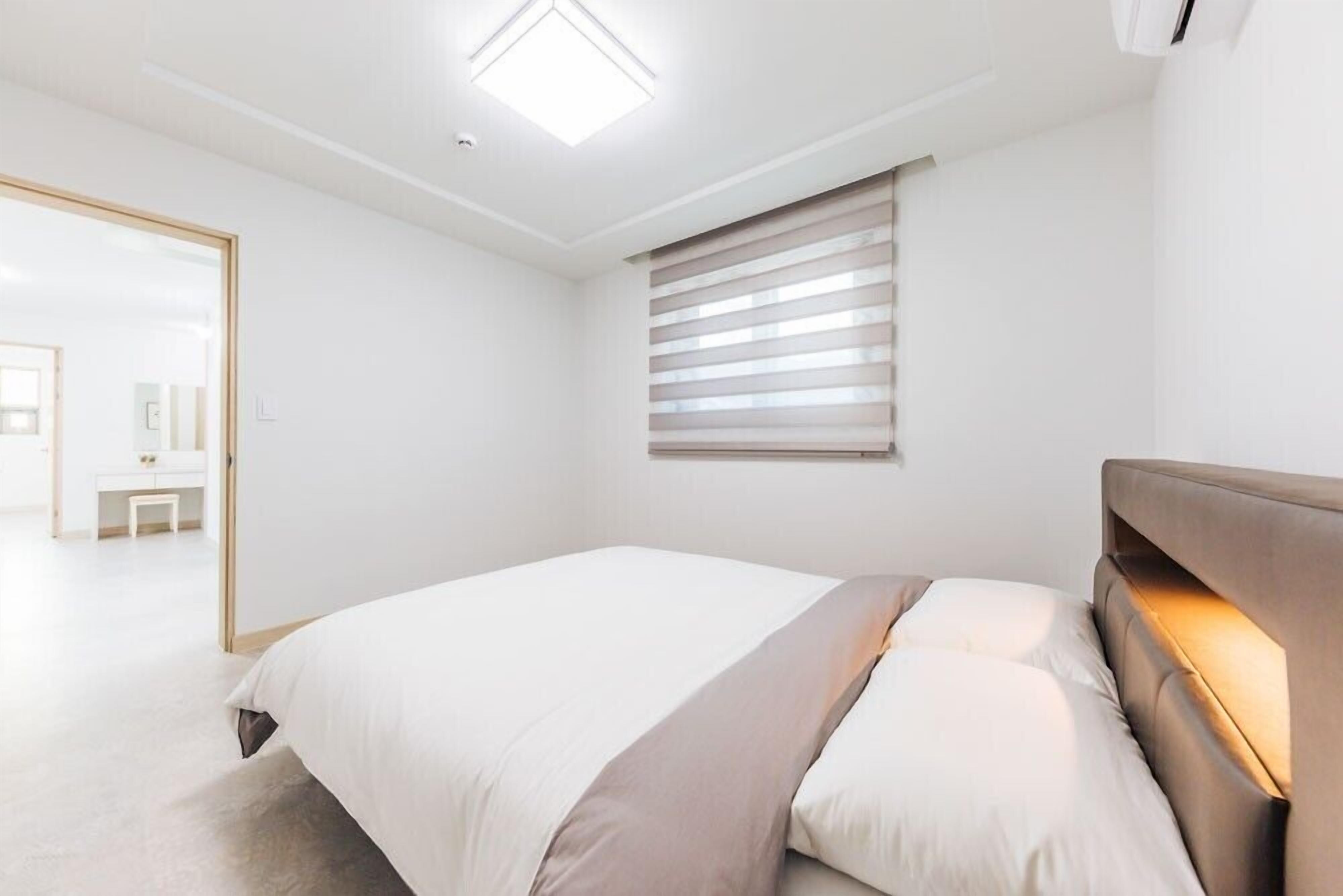 Ein modernes Schlafzimmer mit Bett, Nachttisch, Fenster mit Jalousien und Deckenleuchte.