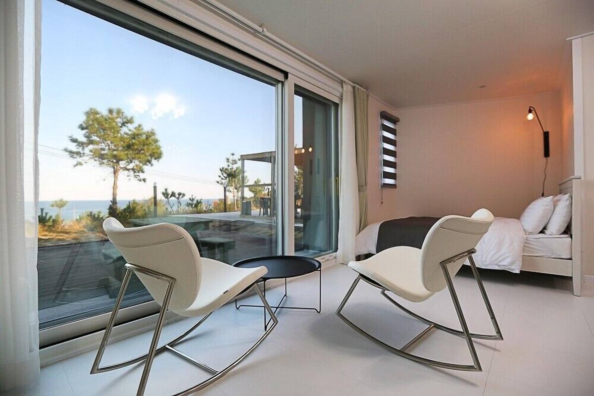 A modern room with a balcony, two rocking chairs, a small table, and a bed.