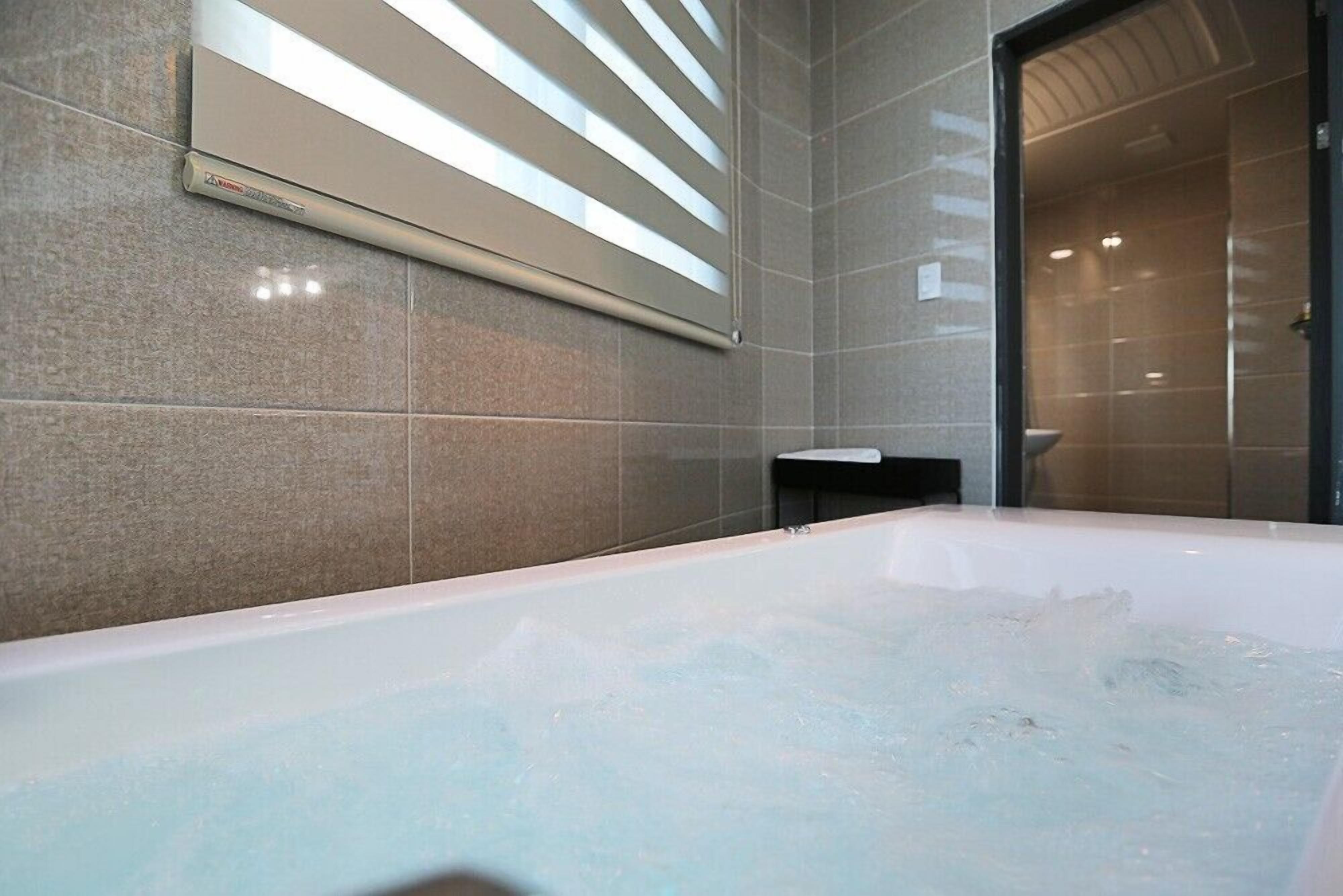 A modern bathroom with a large bathtub, a wall-mounted air conditioning unit, and a glass shower enclosure.