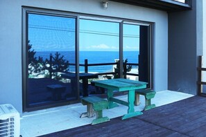 A balcony with a green picnic table and benches, overlooking the ocean.