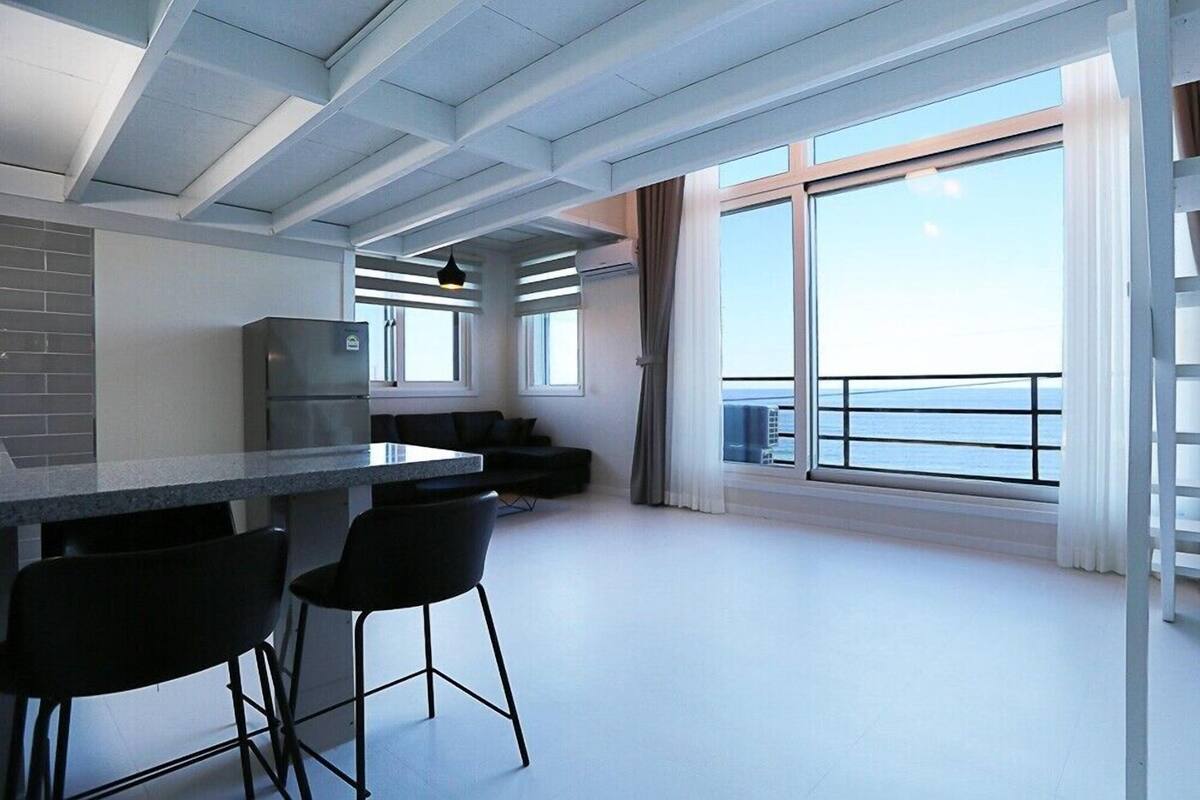 A modern kitchen with a large island, bar stools, and a view of the sea through large windows.