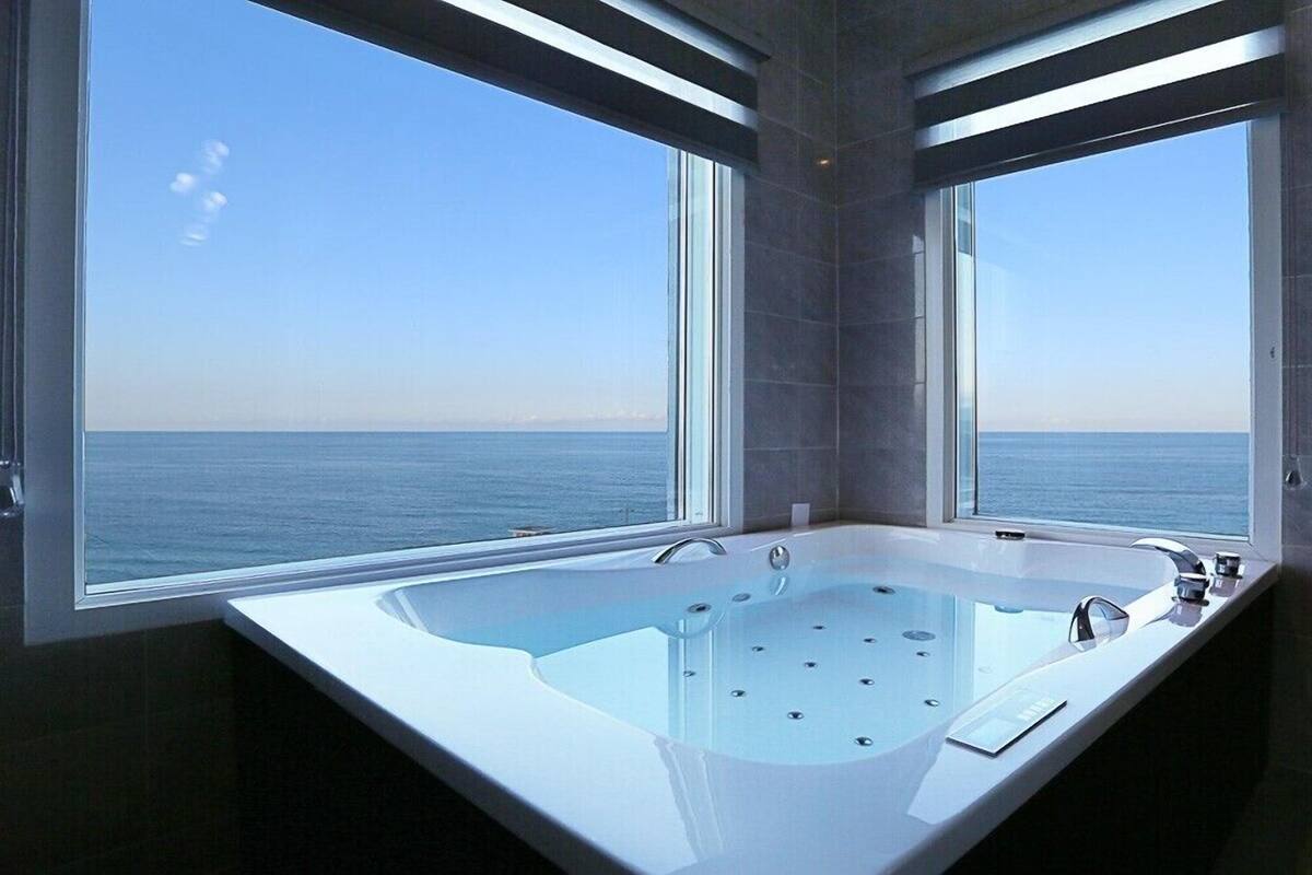 A modern bathroom with a large bathtub and two windows offering a view of the sea.