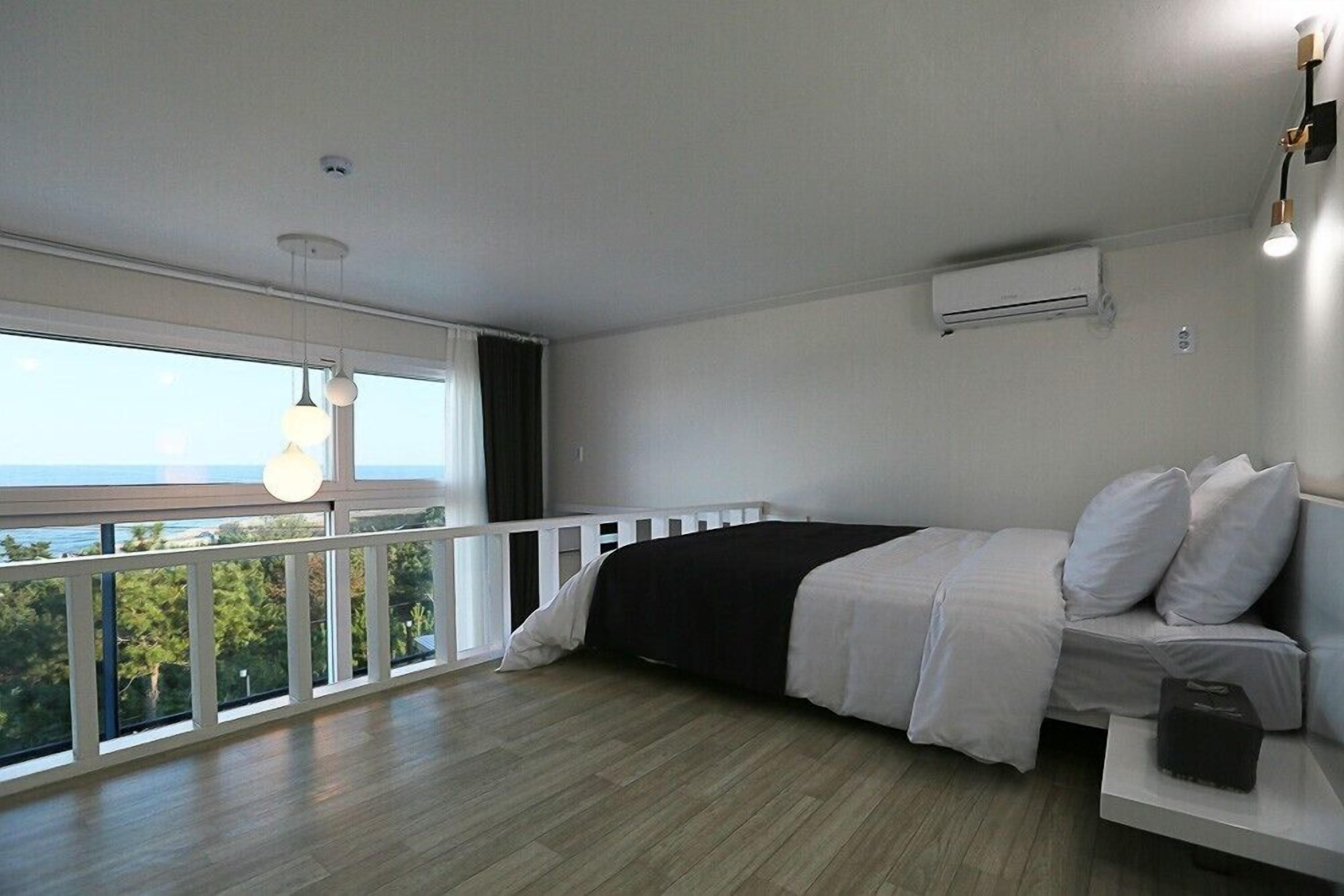 Una camera da letto con balcone, un letto con biancheria bianca, un tavolino consolle bianco e un condizionatore d'aria a parete.