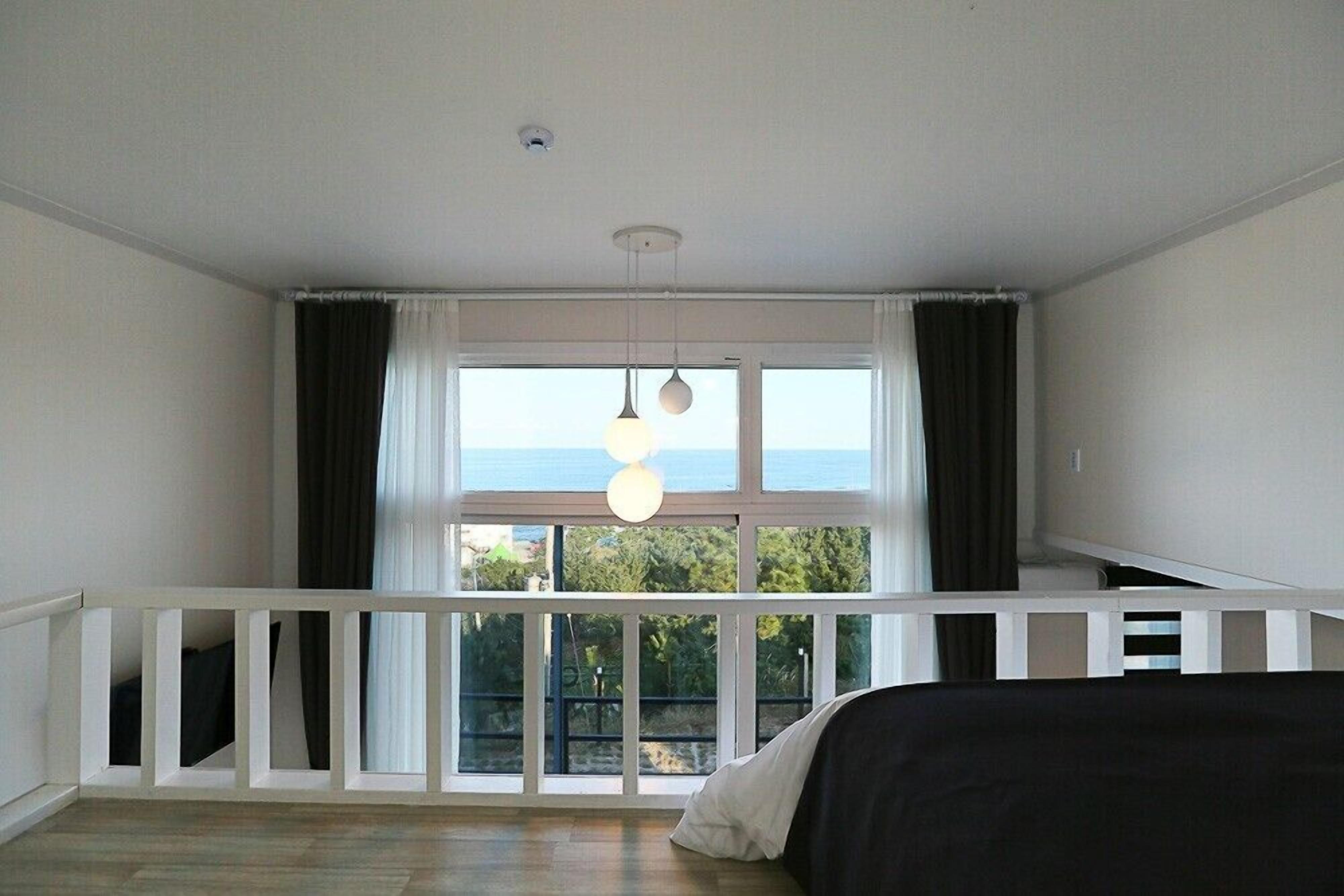 A bedroom with a large window, a balcony, and a hanging light fixture.