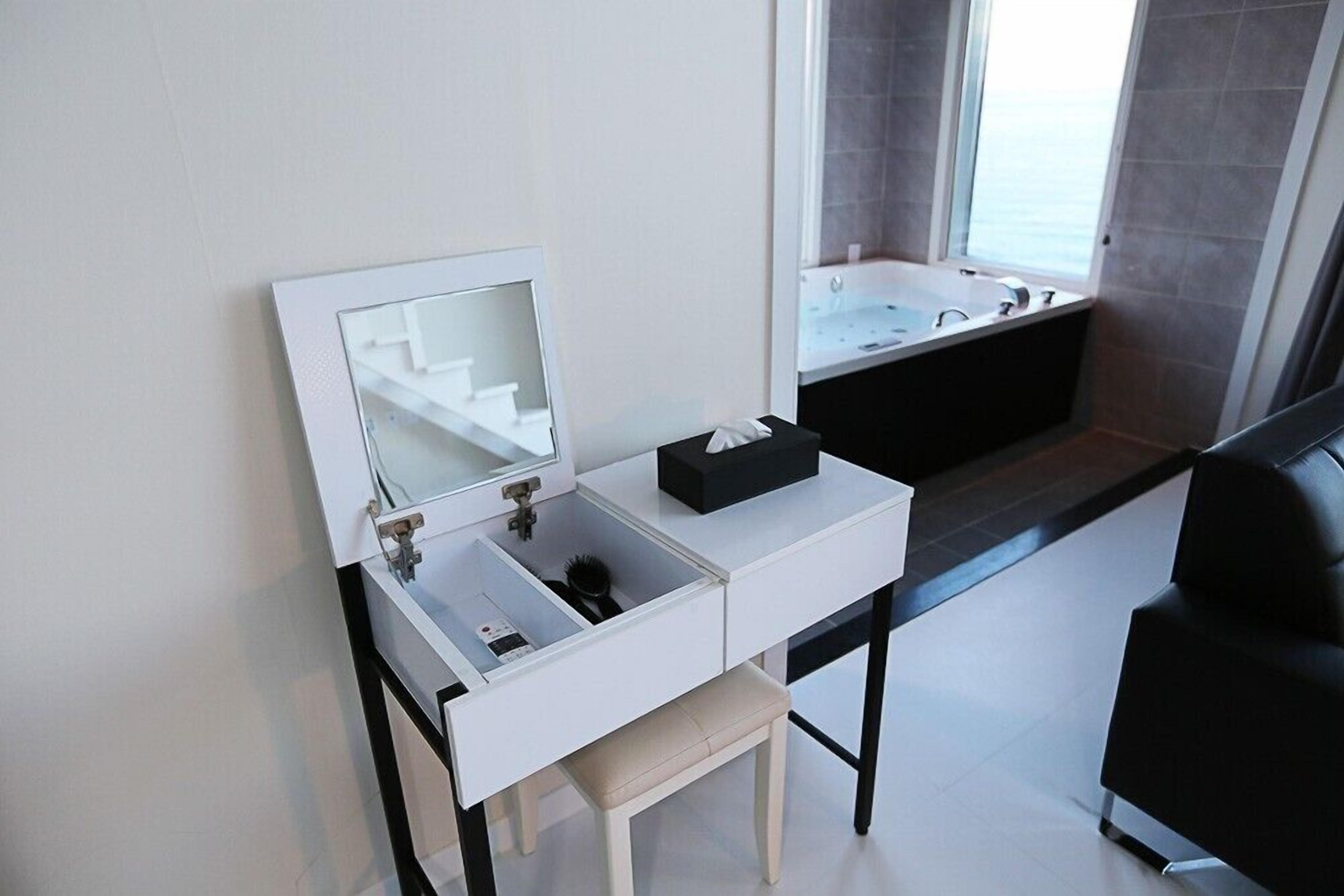 Une salle de bain moderne avec un meuble-lavabo blanc, un grand miroir, une boîte noire et une baignoire visible à travers une fenêtre.