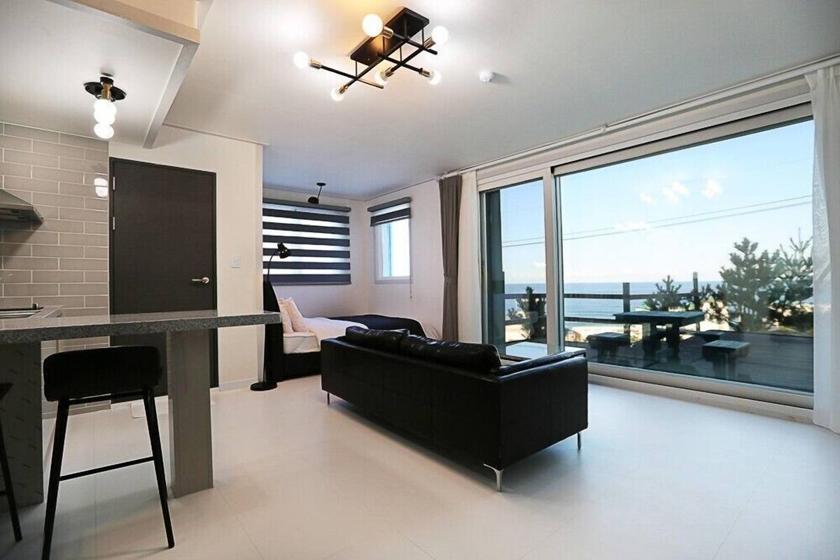 A modern living space with a kitchen, a dining area, and a large sliding glass door leading to a balcony with a view of the sea.
