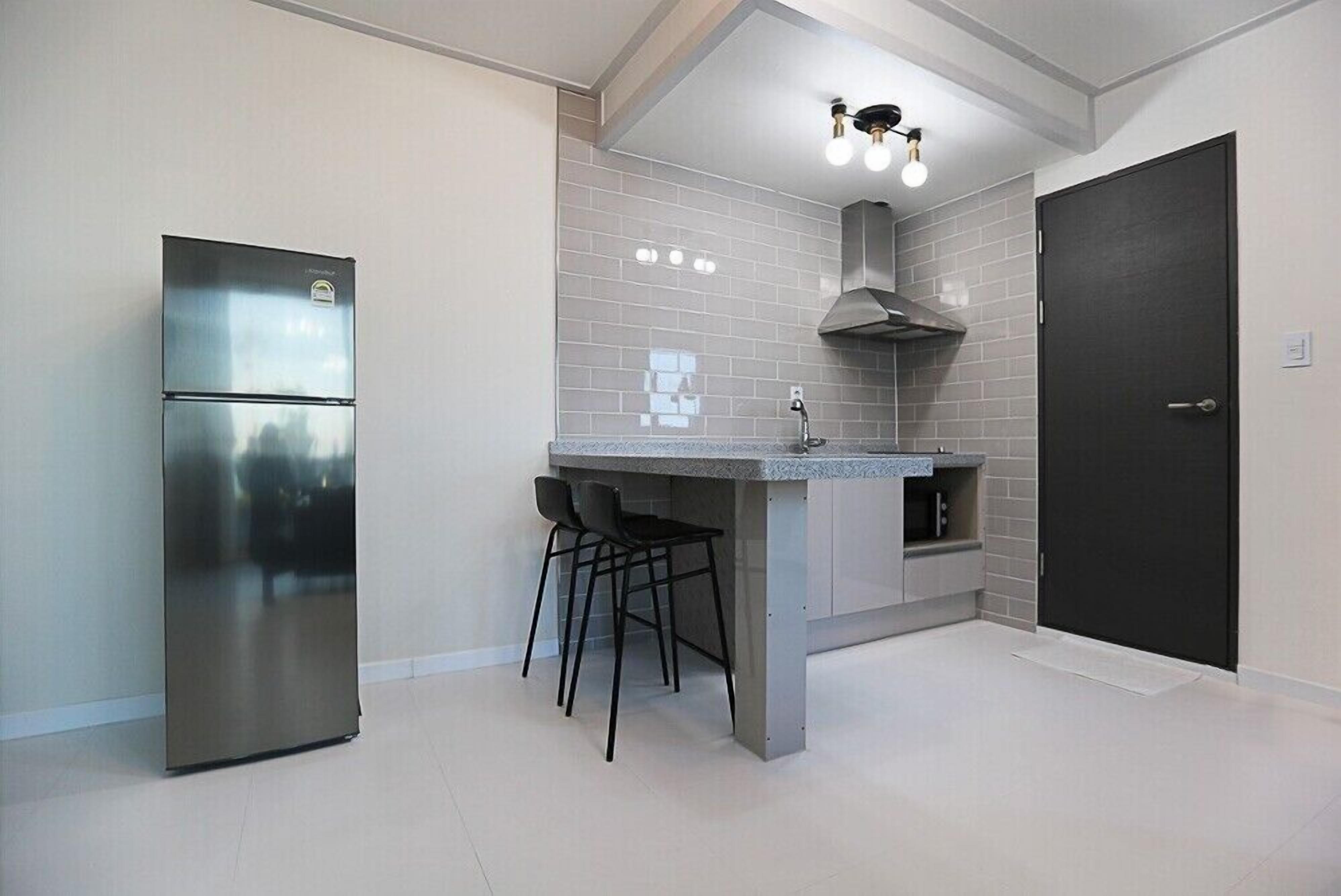 Una cocina moderna con un refrigerador de acero inoxidable, una isla integrada con taburetes de bar y una puerta oscura.