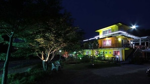 A two-story building with a balcony, surrounded by trees and illuminated by artificial lighting. - Herb Story Pension (Chuncheon)