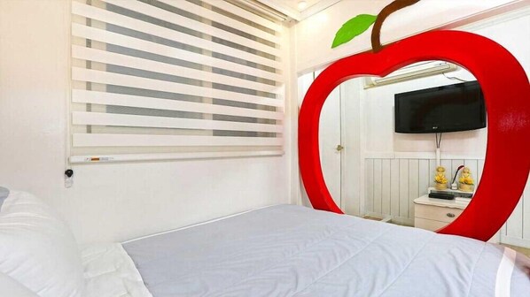 Un dormitorio con una cama, un espejo grande con forma de manzana y un televisor en la pared.