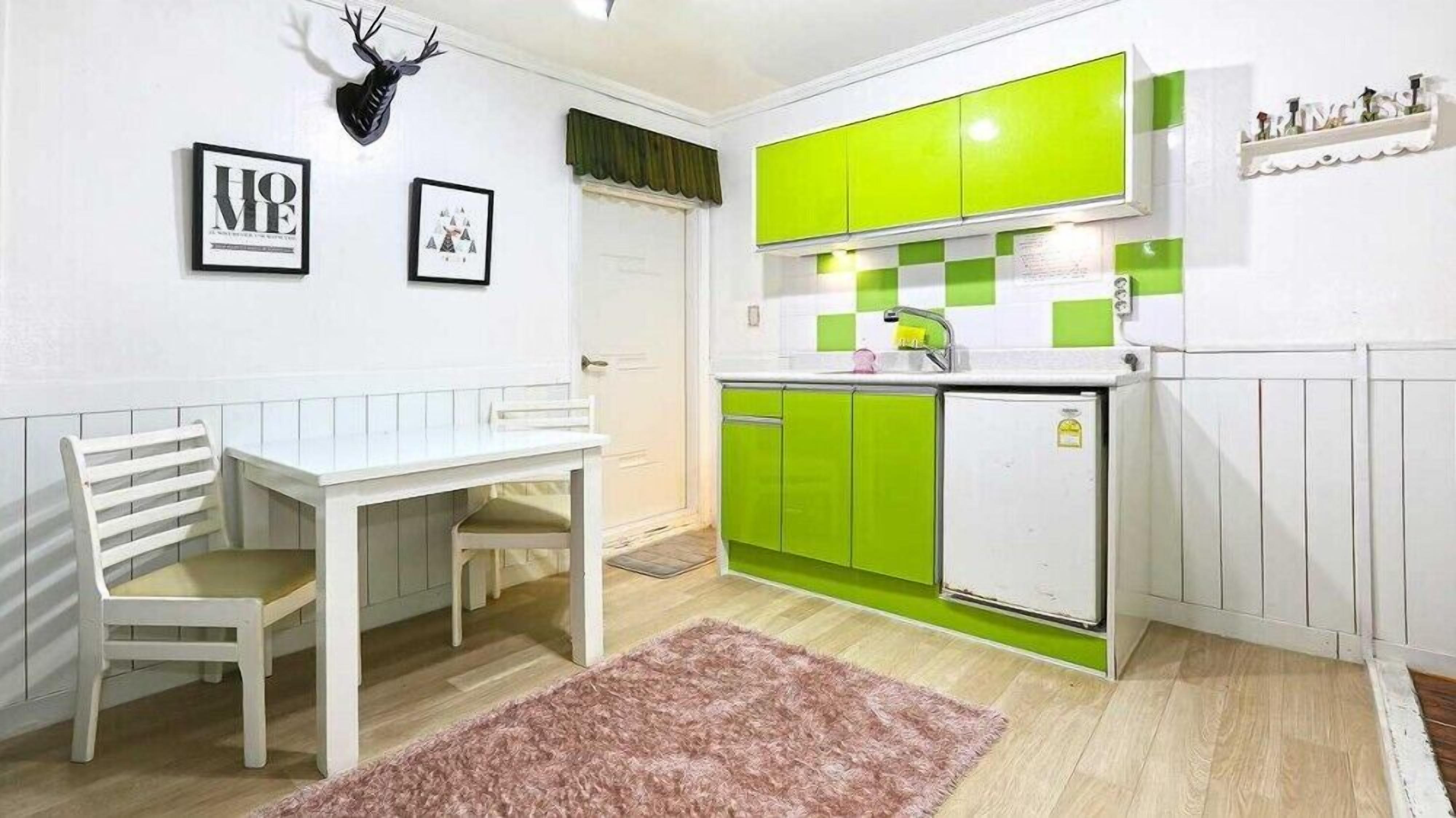 Une cuisine de taille réduite avec des meubles verts, un plan de travail blanc et un petit réfrigérateur.