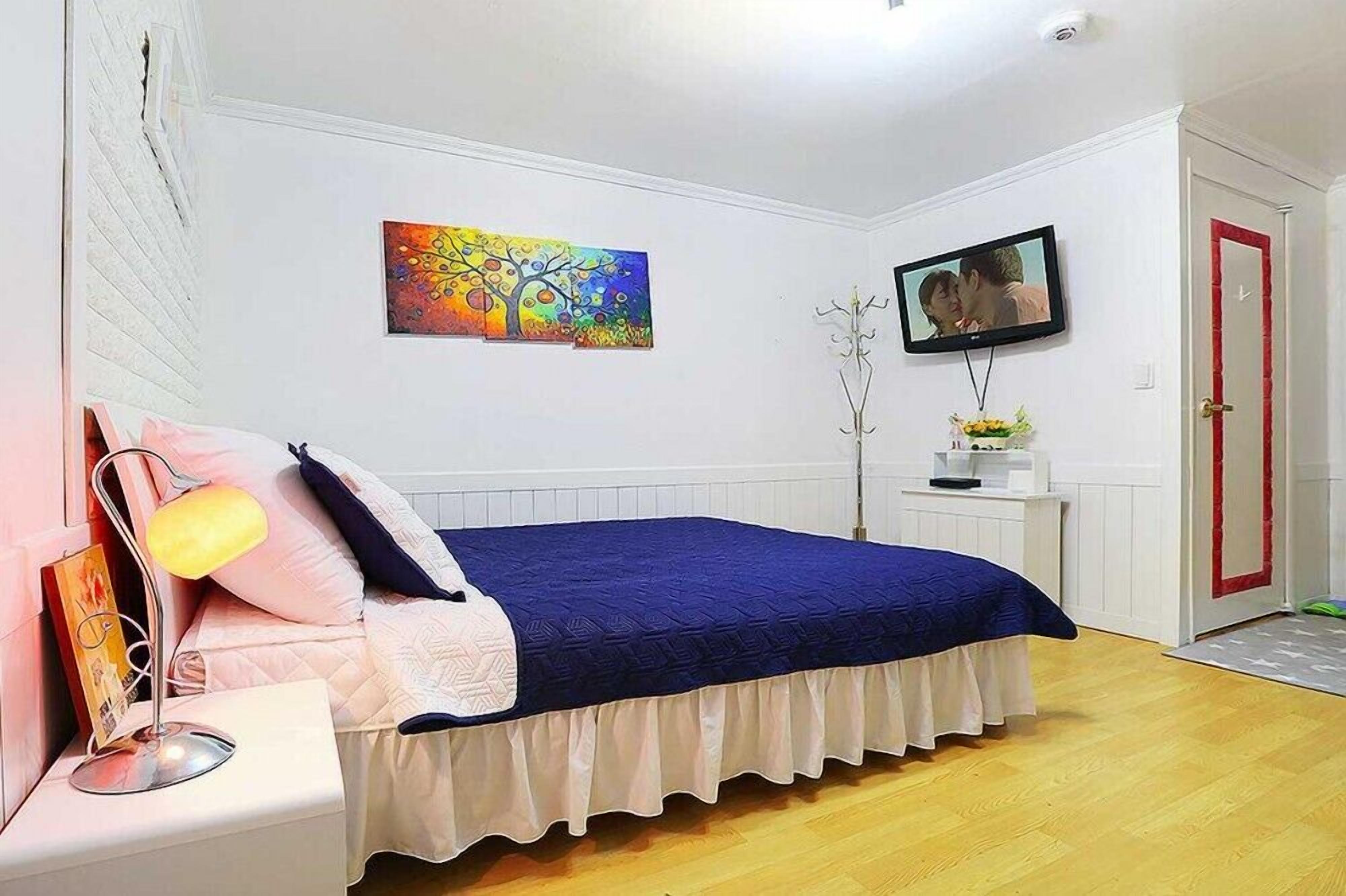 A bedroom with a bed, a nightstand, a TV, and a painting on the wall.