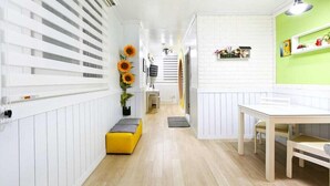 A hallway with white paneling, a yellow bench, a staircase, and a dining area with a green wall and a shelf with decorative items. - Herb Story Pension (Chuncheon)