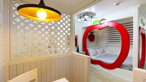 Una habitación con una cama con forma de manzana roja, un separador de celosía blanca y una lámpara colgante.