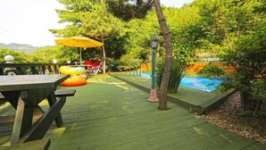 A wooden deck with a pool, surrounded by lush greenery and trees. - Herb Story Pension (Chuncheon)