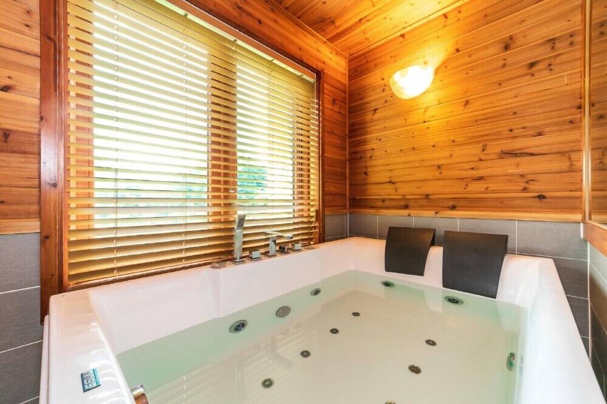 A spa room with a large bathtub, wooden walls, and a window with blinds.