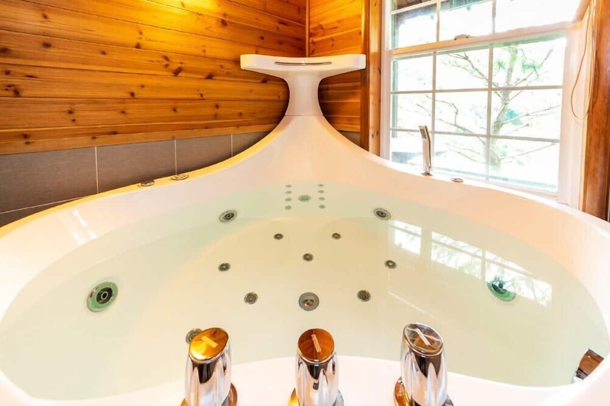 A modern bathroom with a freestanding bathtub, wooden walls, and a window with a view of trees.
