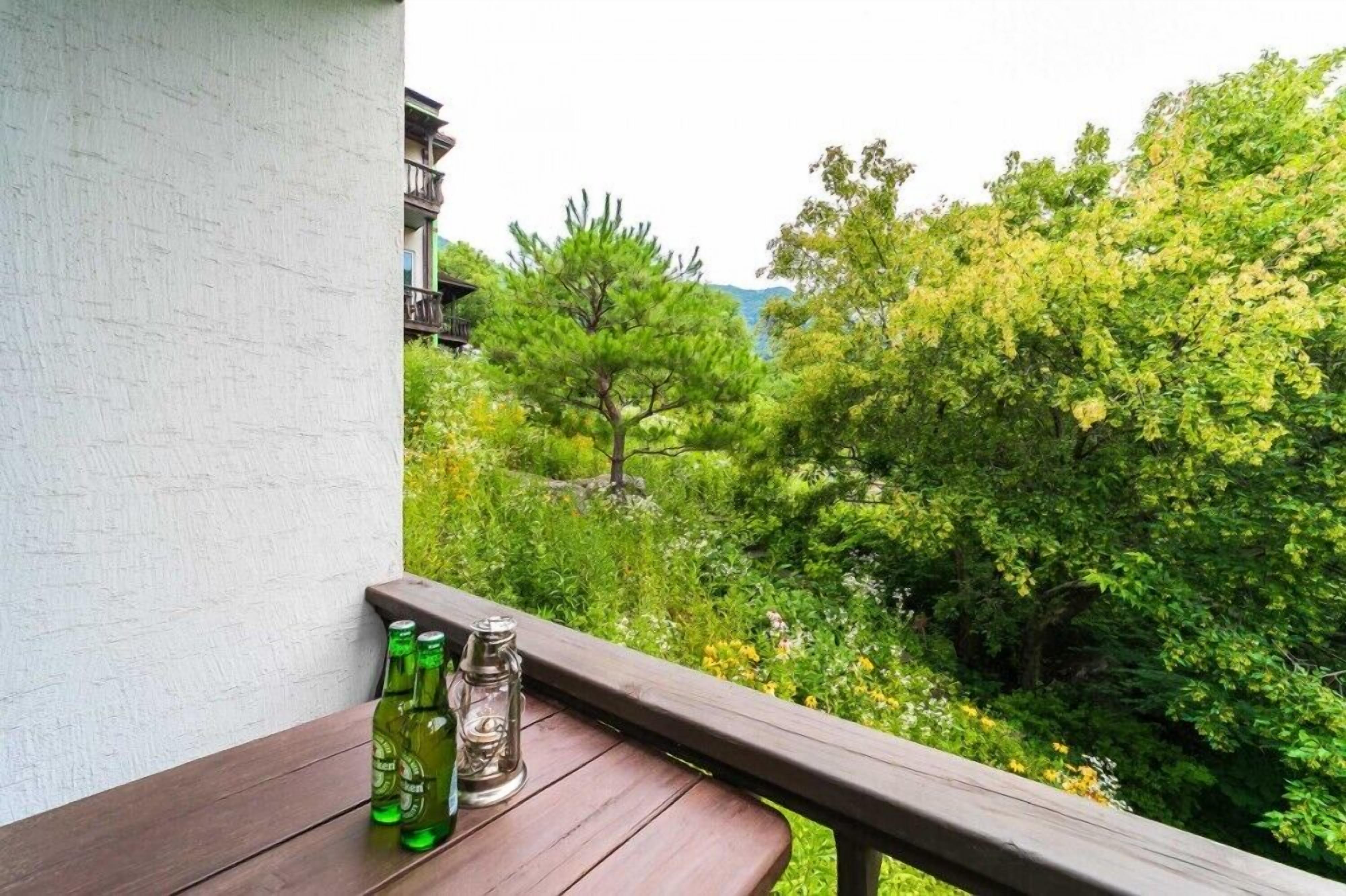 A balcony with a wooden table, two green bottles, and a glass bottle.