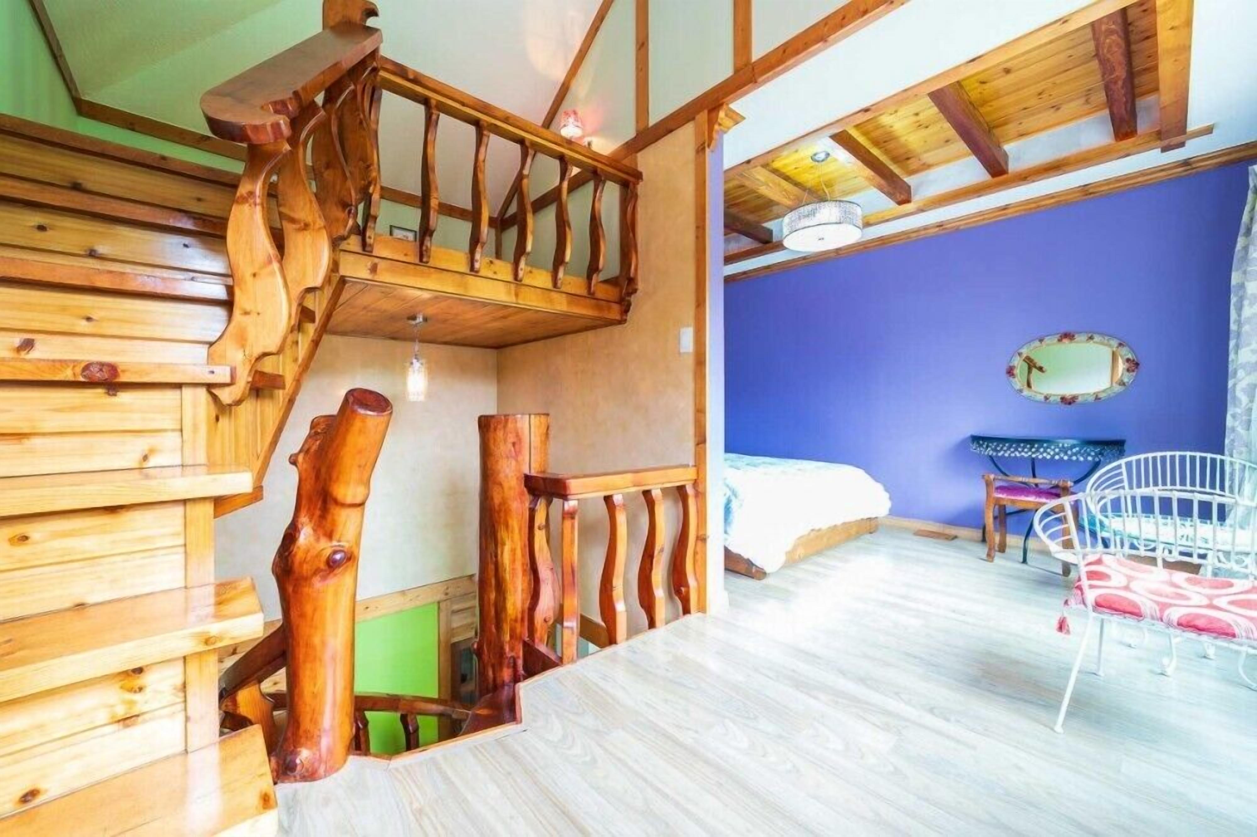 Una escalera de madera con barandilla lleva a un dormitorio con pared azul y una cama.