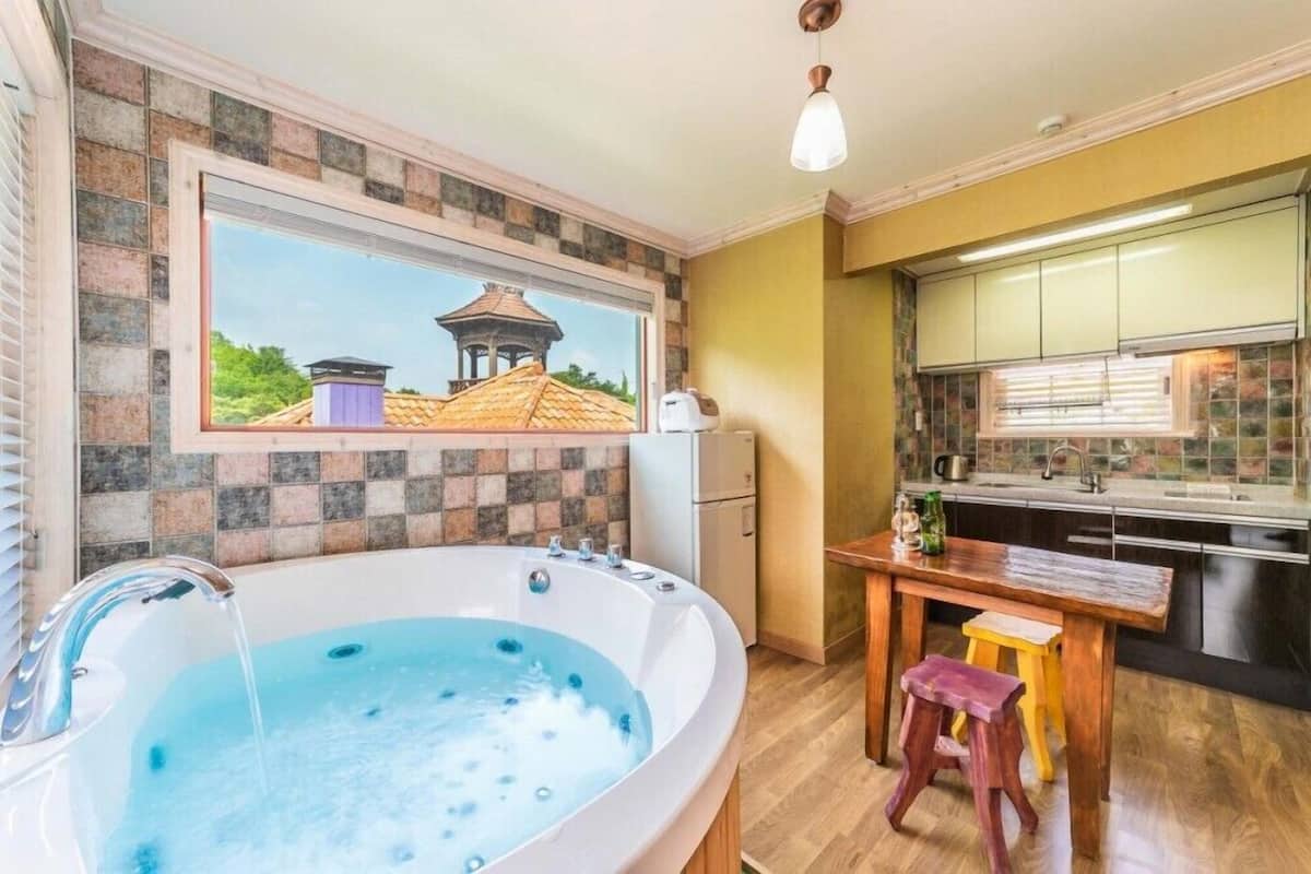 A bathroom with a large bathtub, a window with a view of a gazebo, and a wooden stool.