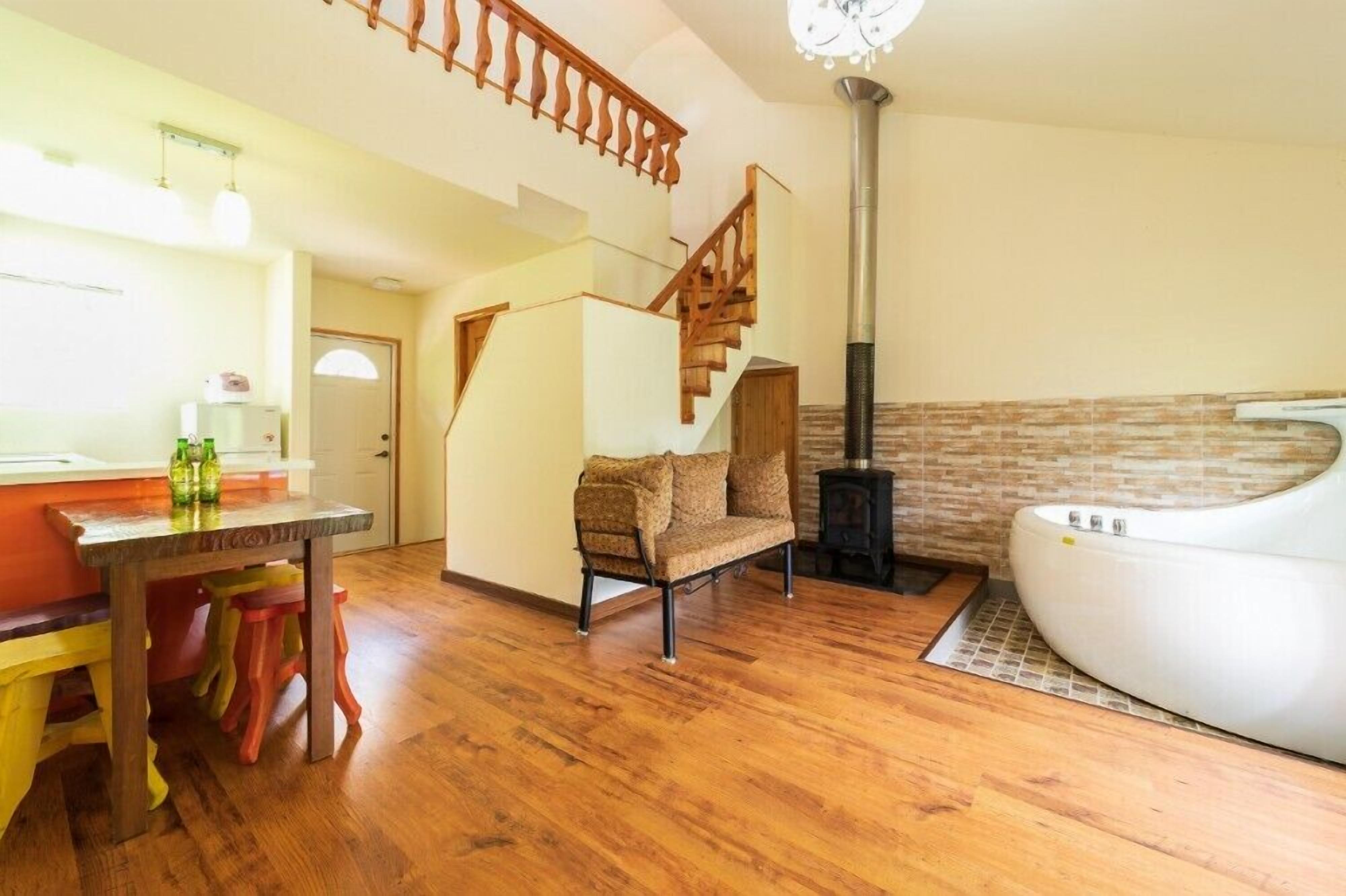 A cozy living room with a wooden staircase, a sofa, a table with colorful stools, and a white bathtub.