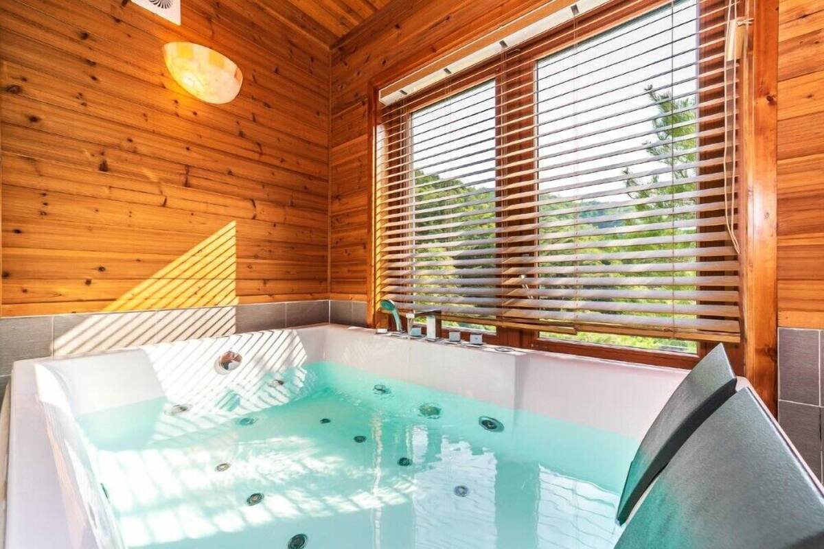 A wooden cabin with a hot tub, wooden walls, and a window with blinds.