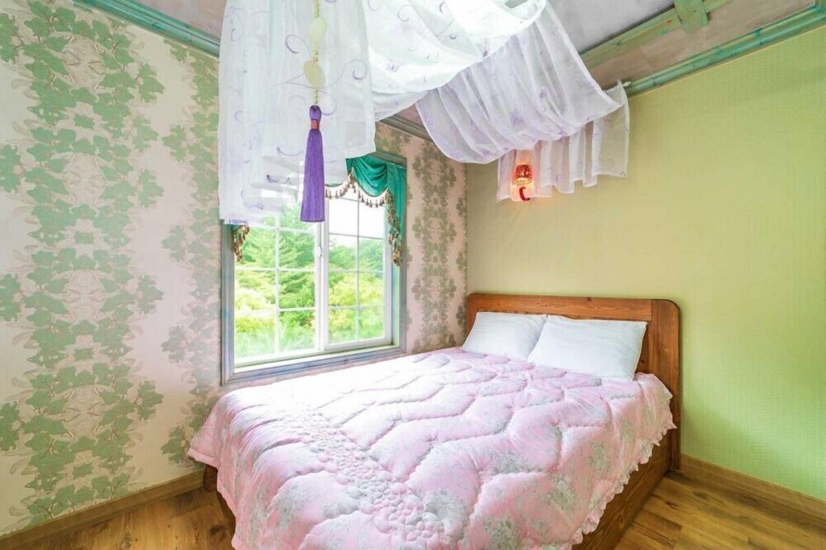 A bedroom with a wooden bed, a window with a view of greenery, and a decorative canopy.
