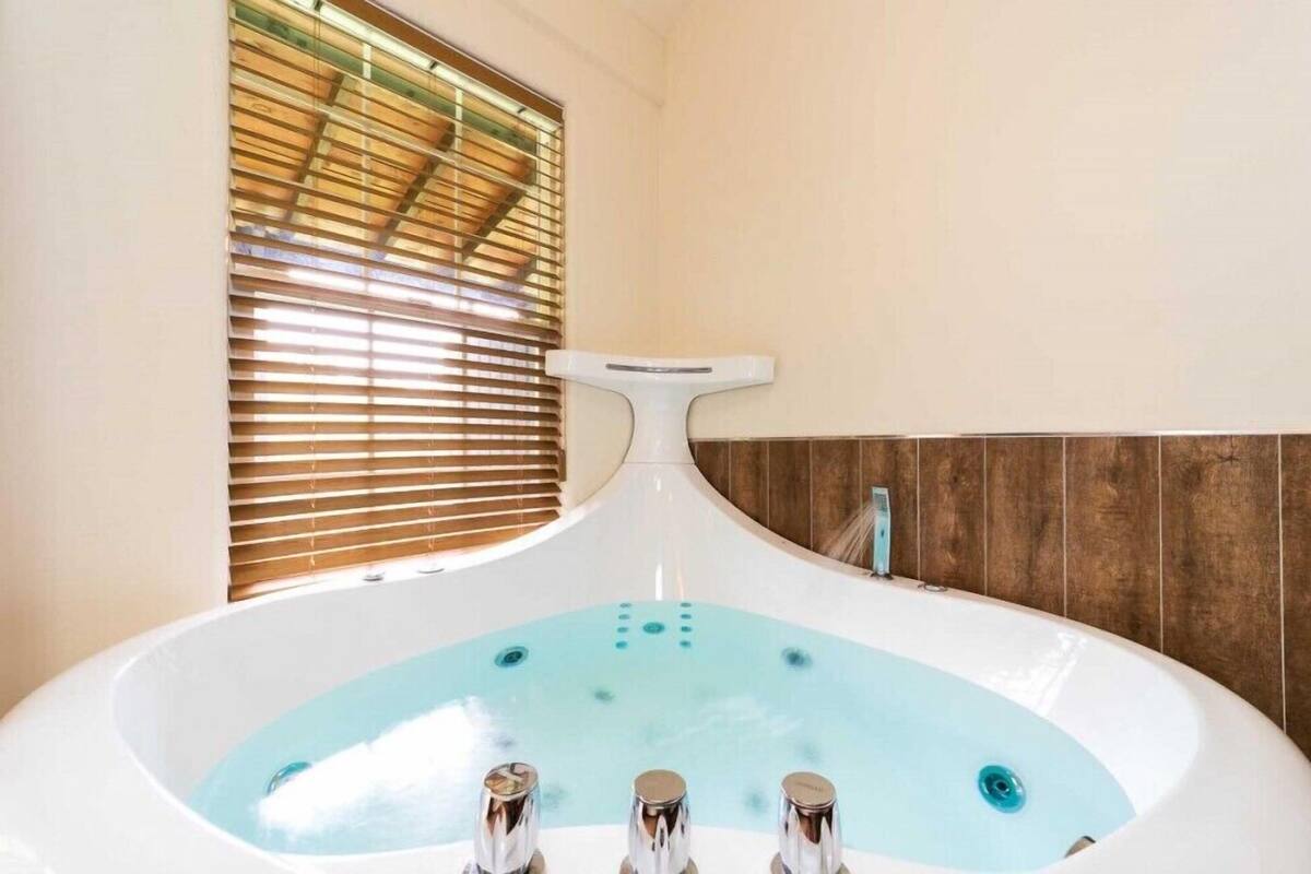 A modern bathroom with a freestanding bathtub, wooden paneling, and a window with blinds.