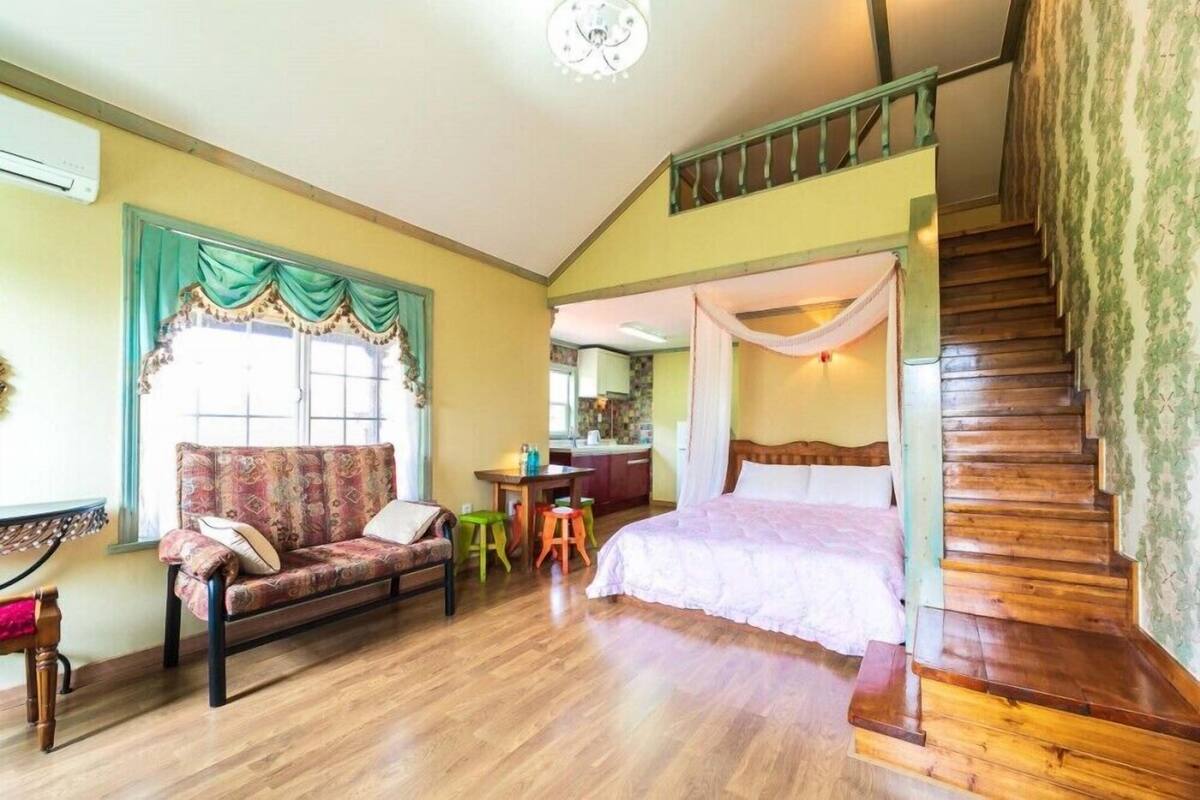 A room with a sofa, a bed, a staircase, and a kitchen area.