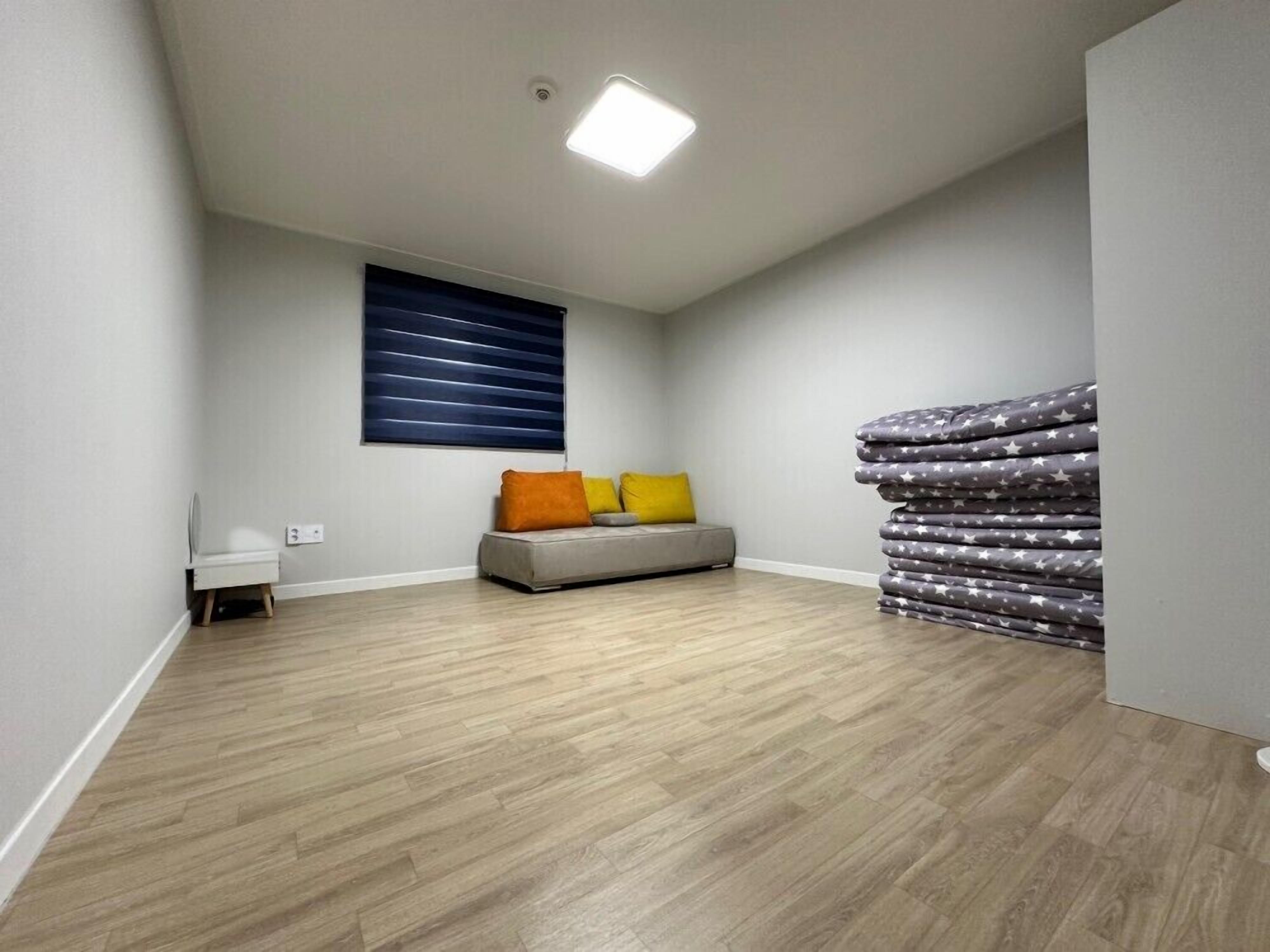 Una habitación con un sofá gris, una ventana con persianas horizontales y un conjunto de ropa de cama con estampado de estrellas.