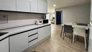 A modern kitchen with white cabinets, a kettle, and a coffee maker. There is a dining area with a table and chairs. - Window to the sky Pension (Gapyeong)