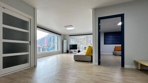 A spacious living room with a large sliding glass door, a sofa, a TV, and a bench. - Window to the sky Pension (Gapyeong)