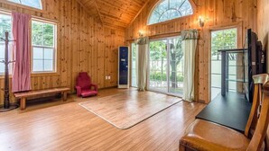 Un interior de madera con un ventanal grande, un banco, una silla roja y un televisor.