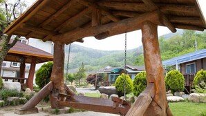 A wooden swing set in a garden with a view of houses and mountains. - Bandi Hwangto Pension (Miryang)