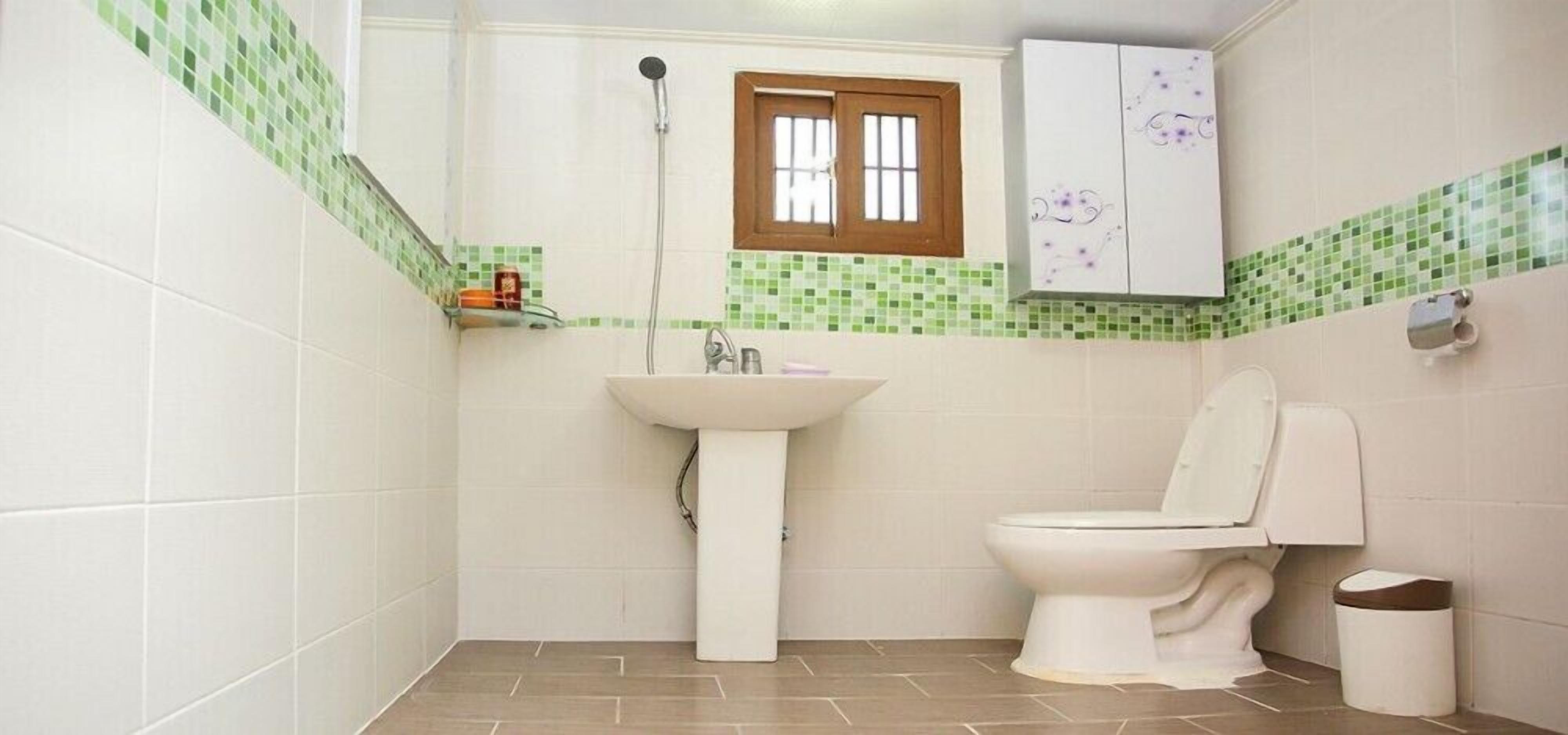 Un baño con lavamanos blanco, inodoro y ventana con marco de madera.