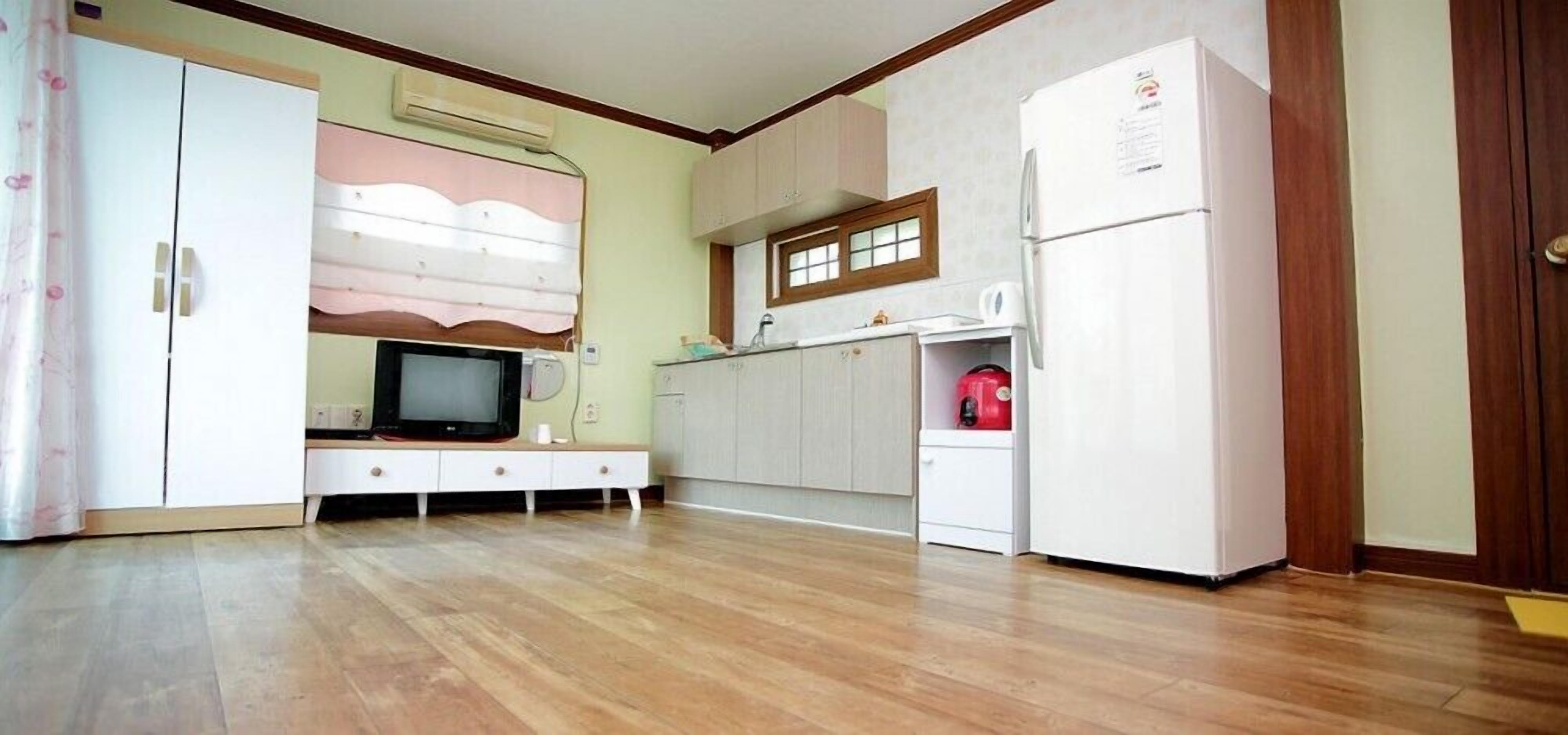 A kitchen with a refrigerator, microwave, and a television on a stand.