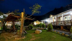 A well-lit outdoor area with a wooden structure, a stone pathway, and neatly trimmed bushes. - Bandi Hwangto Pension (Miryang)