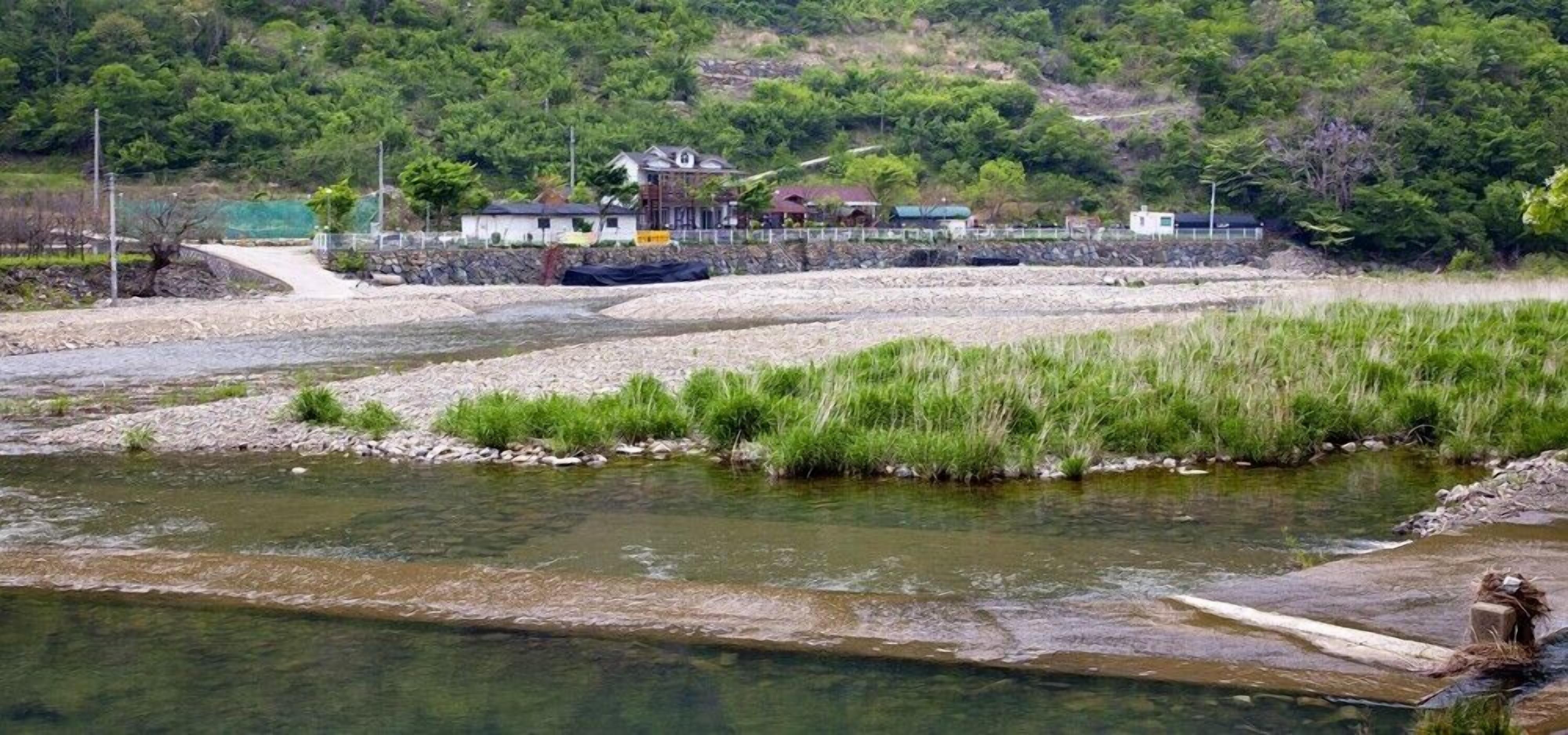 A river with a small bridge, a grassy area, and buildings in the background.