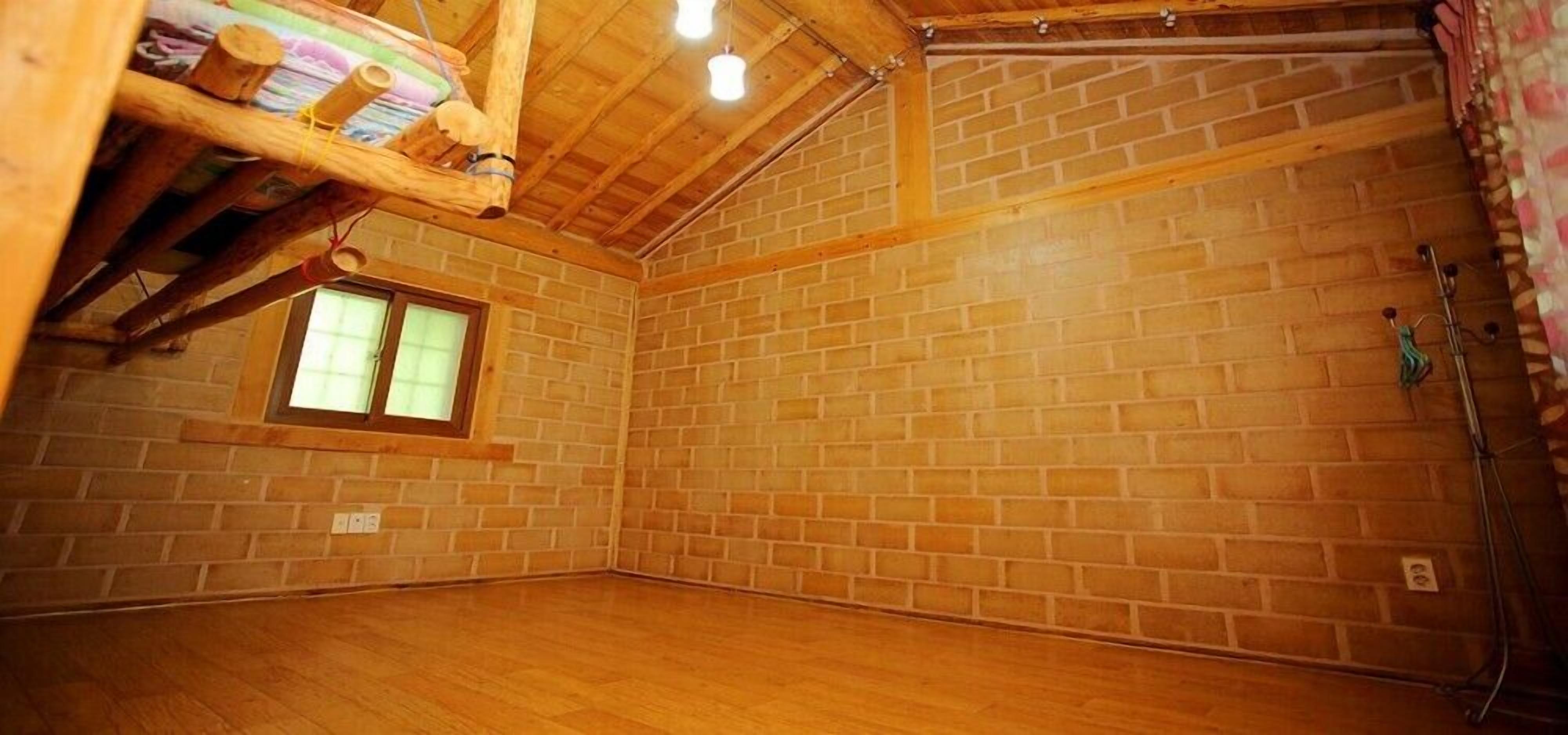 A room with wooden floors, brick walls, a small window, and a wooden beam structure.