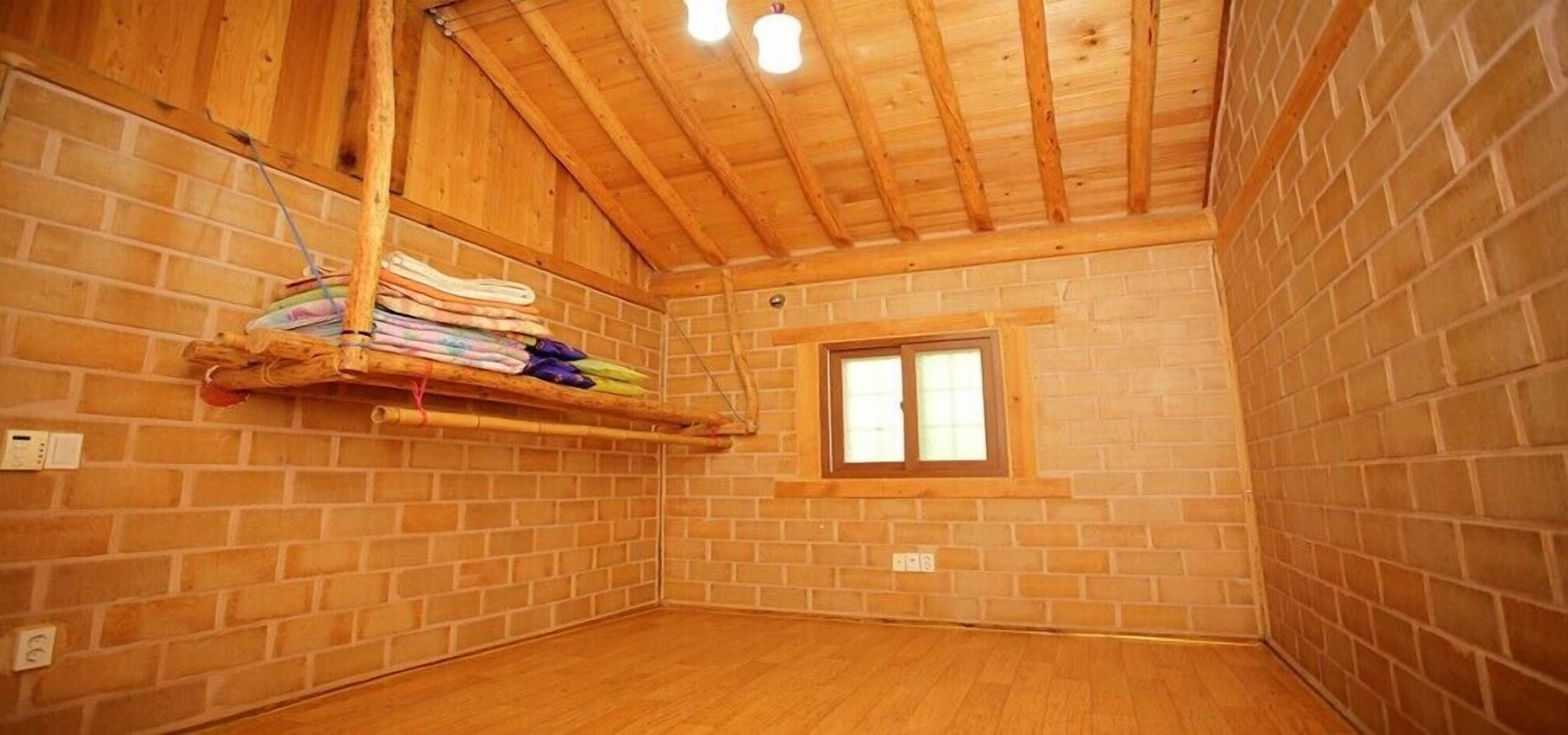 Une pièce avec des poutres apparentes, des murs en briques, une petite fenêtre et un plancher en bois.