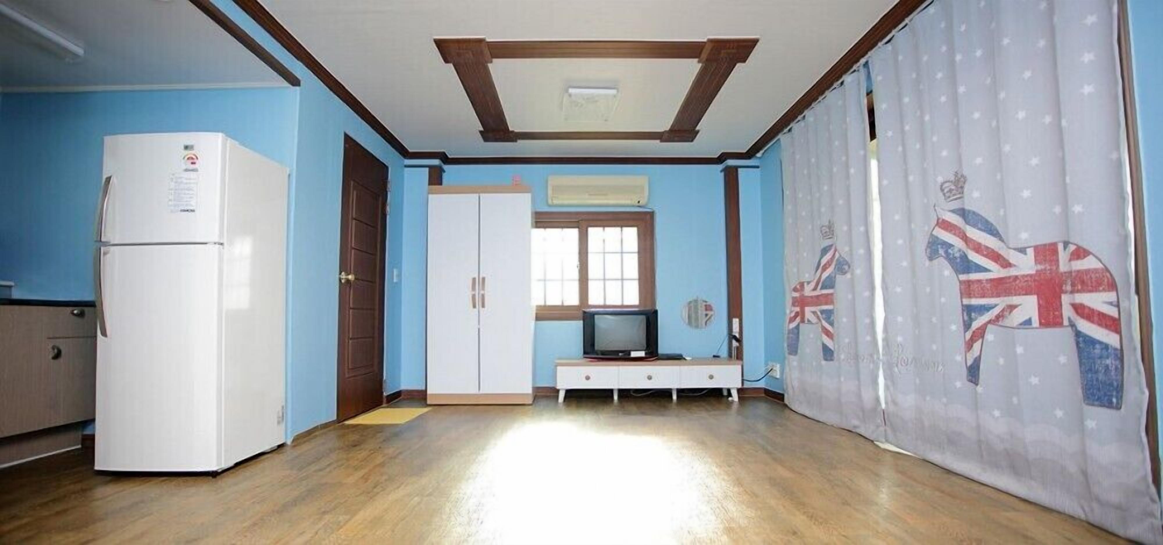 A room with a white refrigerator, a TV on a stand, a wardrobe, and a curtain with a Union Jack design.