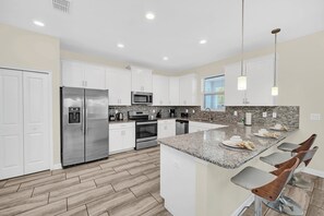 Una cocina moderna con armarios blancos, electrodomésticos de acero inoxidable, encimera de granito y taburetes de bar.