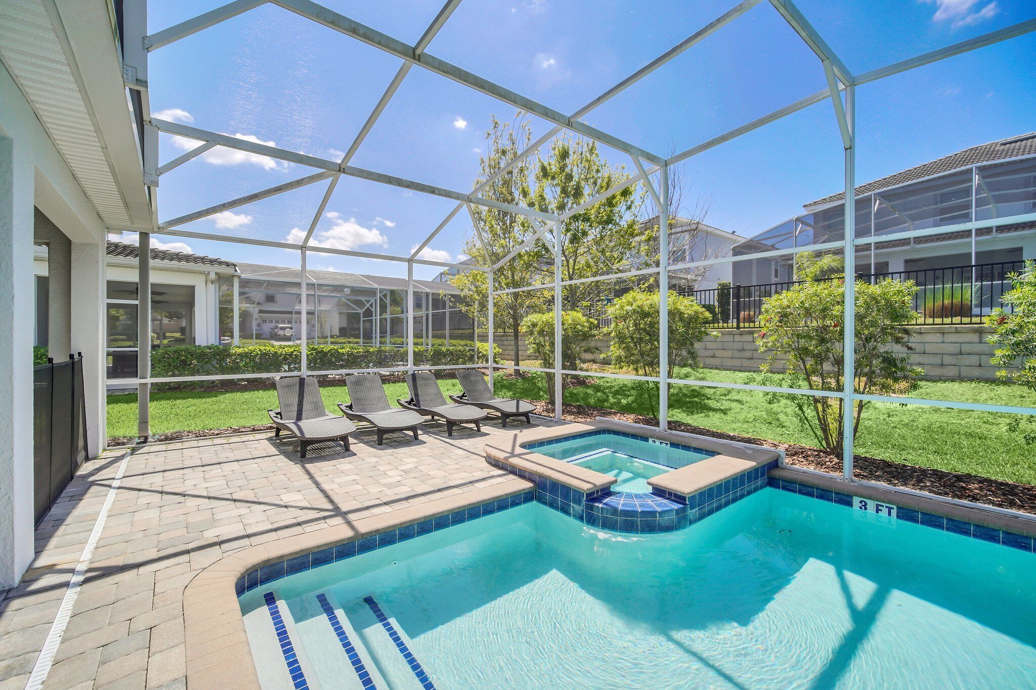 Une piscine dotée d’une structure en verre, de chaises longues et d’une pelouse bien entretenue.