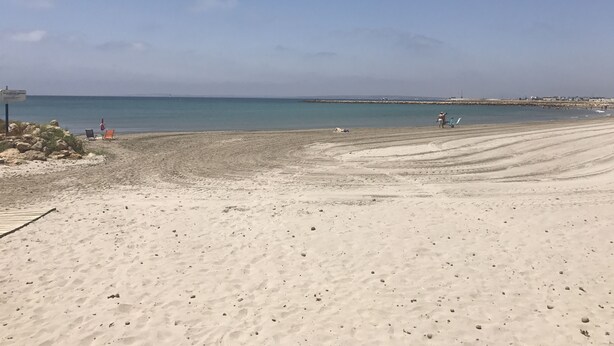 Una platja amb cel serè, sorra daurada i poques persones a la distància.