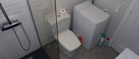 A compact bathroom with a glass shower enclosure, a white toilet, and a compact washing machine.