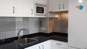Una cuina moderna amb armaris blancs, un taulell negre, microones integrat i rentaplats.