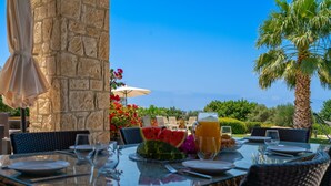 An outdoor dining area with a stone wall, wicker furniture, and a view of the landscape. - Villa 148 - Lofou (Kouklia)