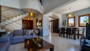 A spacious living area with a modern staircase, a dining area with a table and chairs, and a kitchen in the background. - Villa 148 - Lofou (Kouklia)